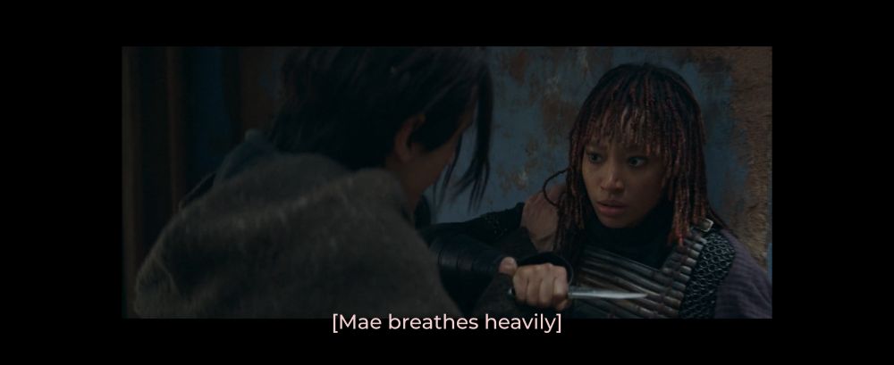 Mae has her back against a wall and has an expression of shock. She holds a small knife in her hand.

Qimir has a hand on her shoulder, pushing. His other hand is around Mae's knife-wielding hand. 

The subtitle reads "[Mae breathes heavily]"