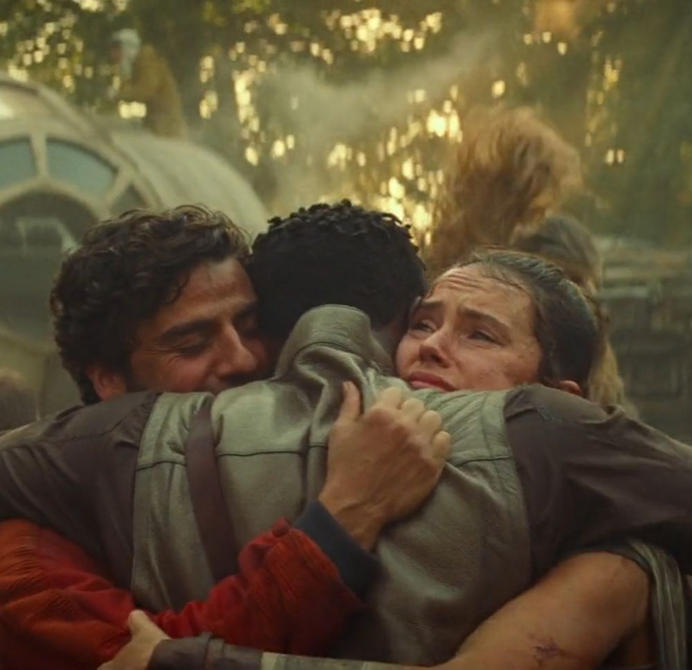 Poe, Finn and Rey hugging. Poe is smiling and looks happy. Rey is not smiling, she looks pained. Finns expression cannot be seen.