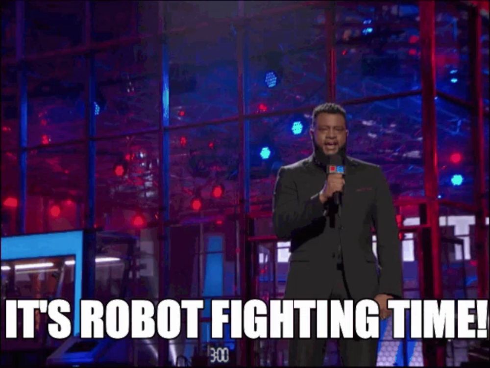 a man with a beard is holding a microphone and says it 's robot fighting time