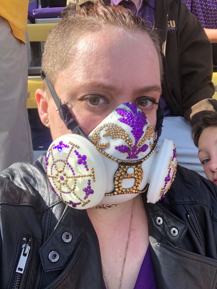 Alc in a black leather jacket and a white respirator bedazzled in purple and gold crystals for LSU tailgating 