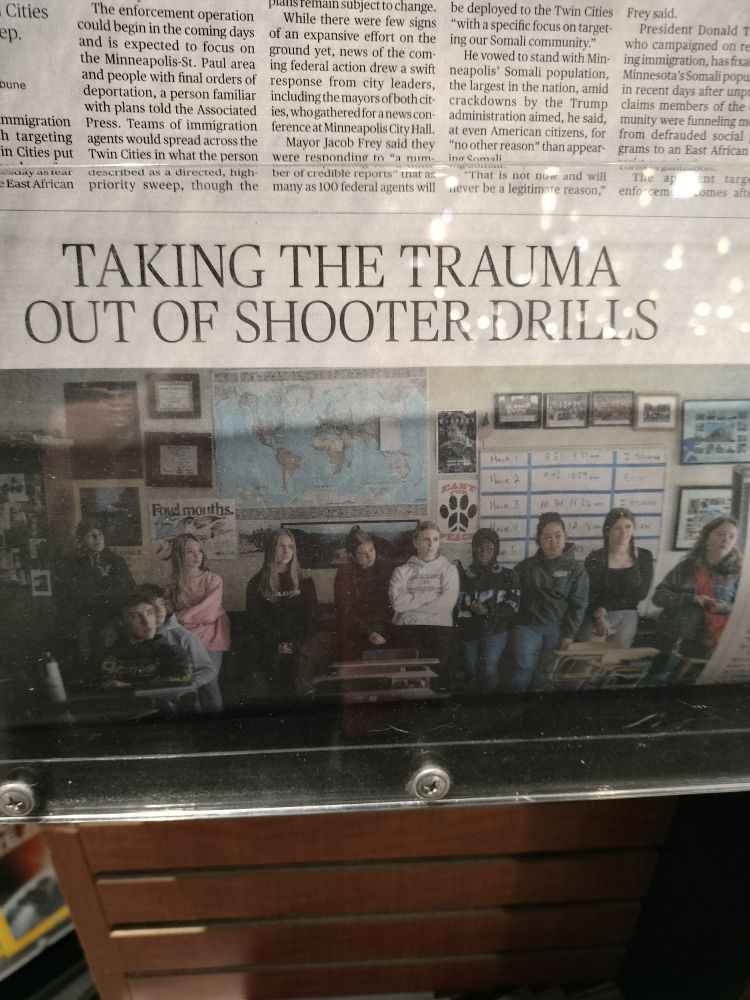 A newspaper headline reading "Taking The Trauma Out of Shooter Drills" over a photograph of a classroom full of children.