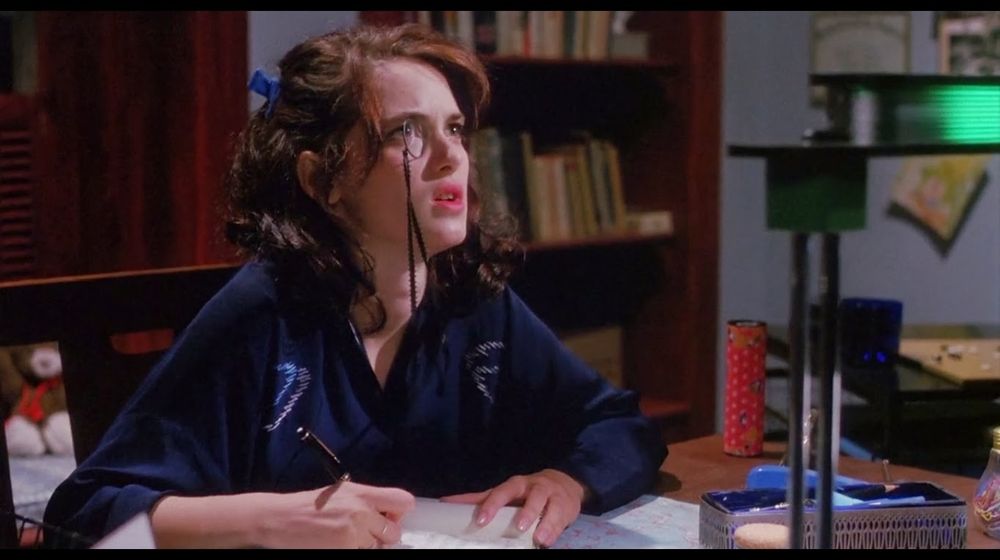 character Veronica Sawyer from the movie "Heathers," sitting at her desk and writing in her journal 