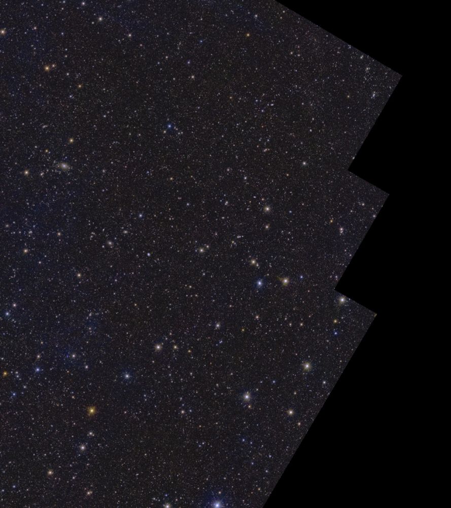 On a black background lies a rectangular shape with several stepped notches cut out of its corners, oriented with its longest edges running from bottom left to top right. Contained within the shape are more than ten million galaxies, and stars of various size, brightness and colour. Wispy faint blue cloud-like structures permeate the image, representing gas and dust in between the stars in our own galaxy.