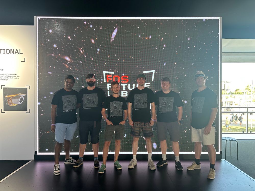 Our evening shift Euclid team, 6 of us, smiling for the camera in front of a large LED screen showing a Euclid image.