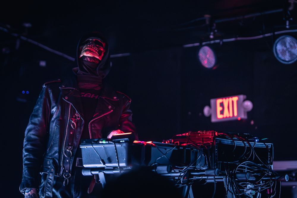 One member of musical act Gost performing at X-Ray Arcade in Milwaukee, WI; his head is thrown back as he operates electronic music equipment. The room is dimly lit with dramatic red lighting accents.
