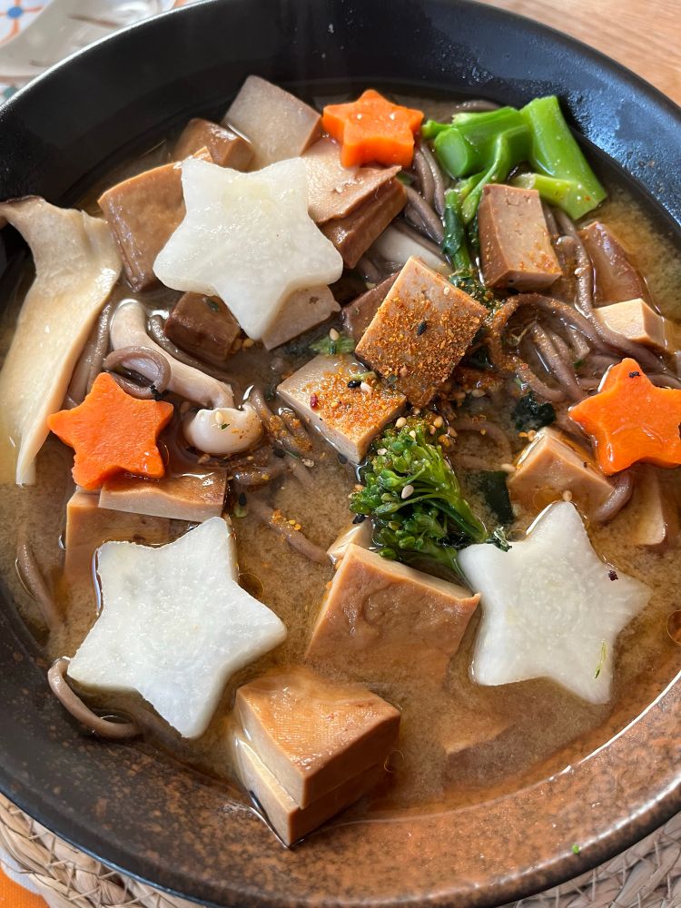 A bowl of miso soba with big white daikon stars, little orange carrot stars, broccoli, mushrooms and squares of five spice tofu 
