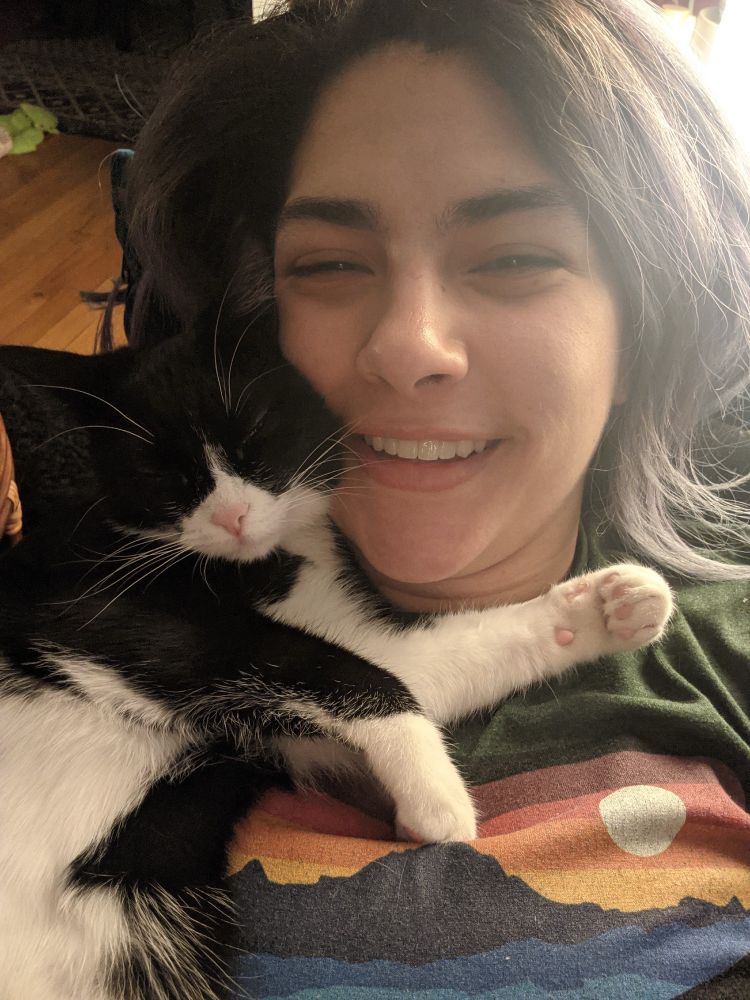 Roll, a very happy tuxedo cat with a pink nose cuddled up with Lena. Both Lena and Roll are smiling!