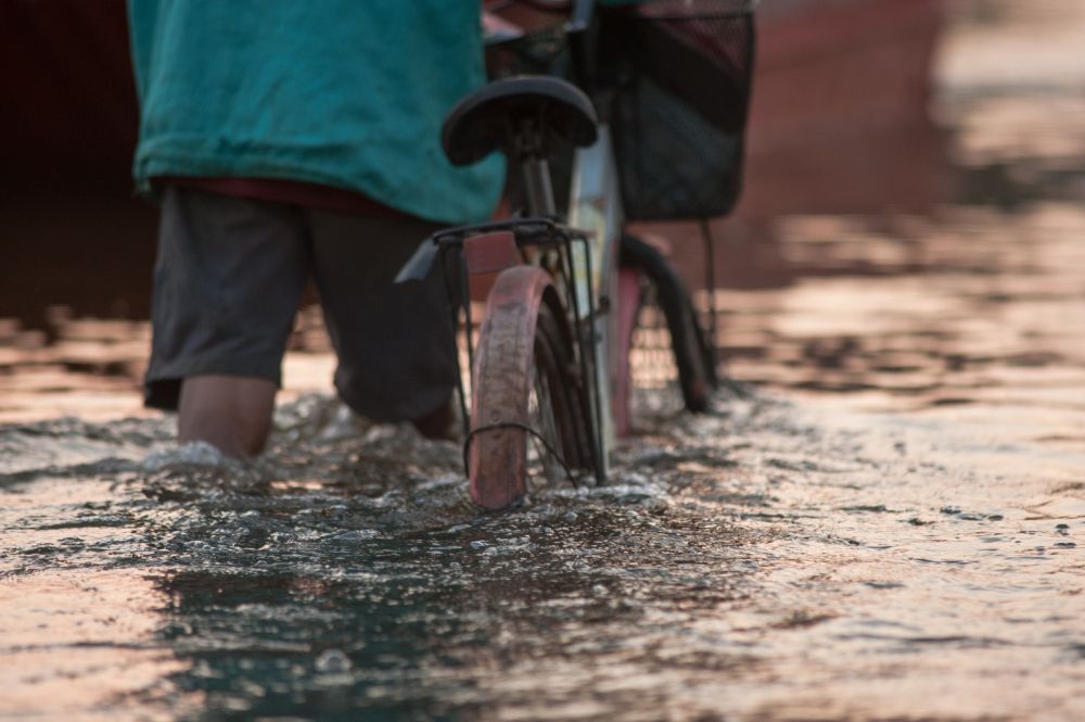 Un homme pousse son vélo dans une rue innondée.