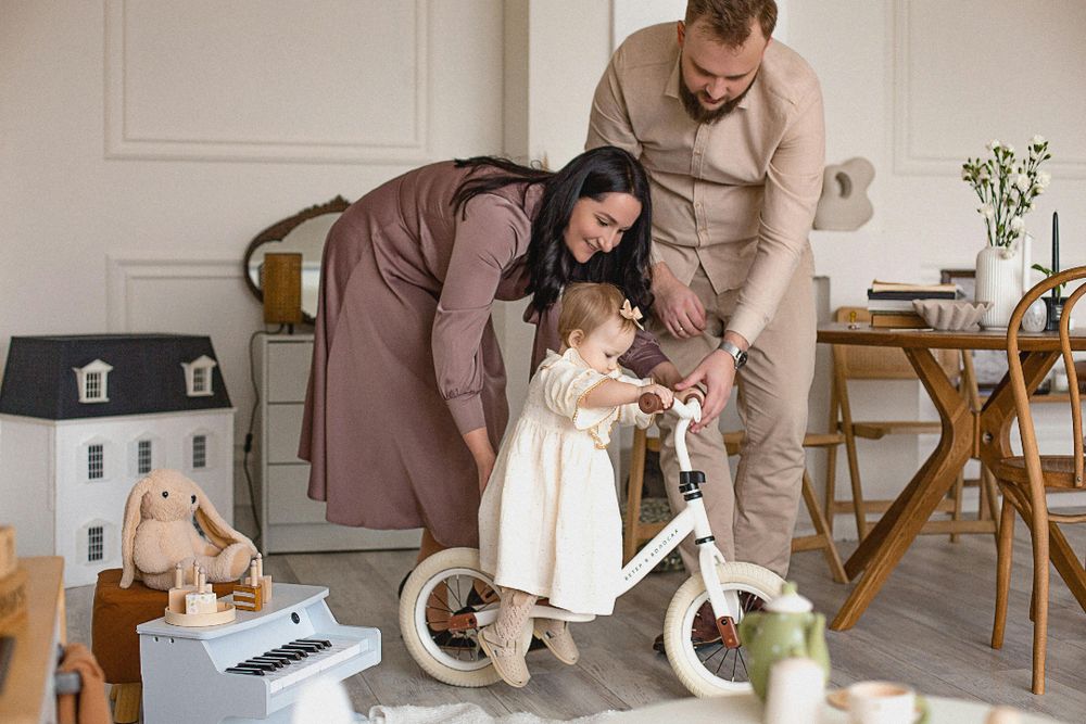 A man and woman are standing in a room with a child on a bike