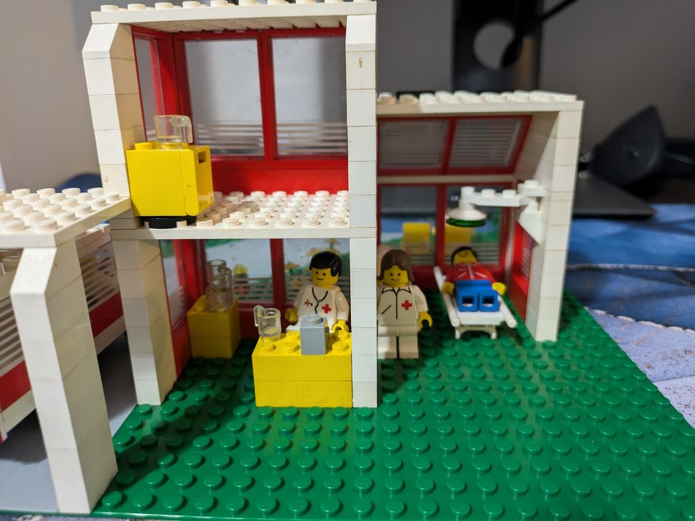 Lego hospital interior showing a patient in an operating room with a doctor while the nurse charts at the desk