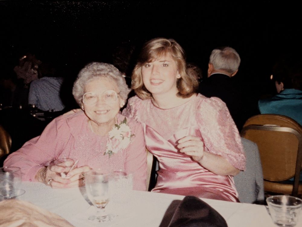 An older lady and a young woman wearing pink dresses sit together at a table