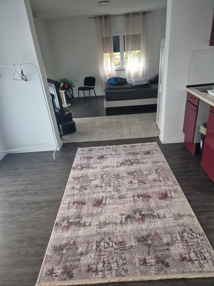 Blick vom Eingang des zimmers auf das Bett rechts ne kleine Küche am Boden 2 tepische