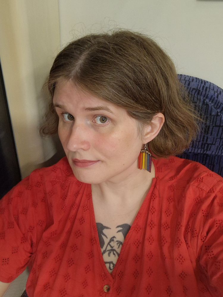 Selfie of me on a train, I'm wearing a red dress and rainbow earrings