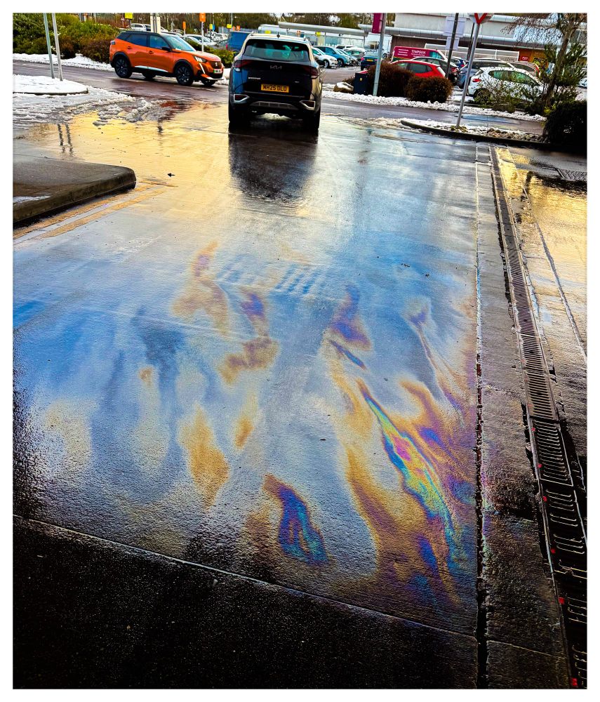 Petrol station forecourt with iridescent fuel spills resembling flames
