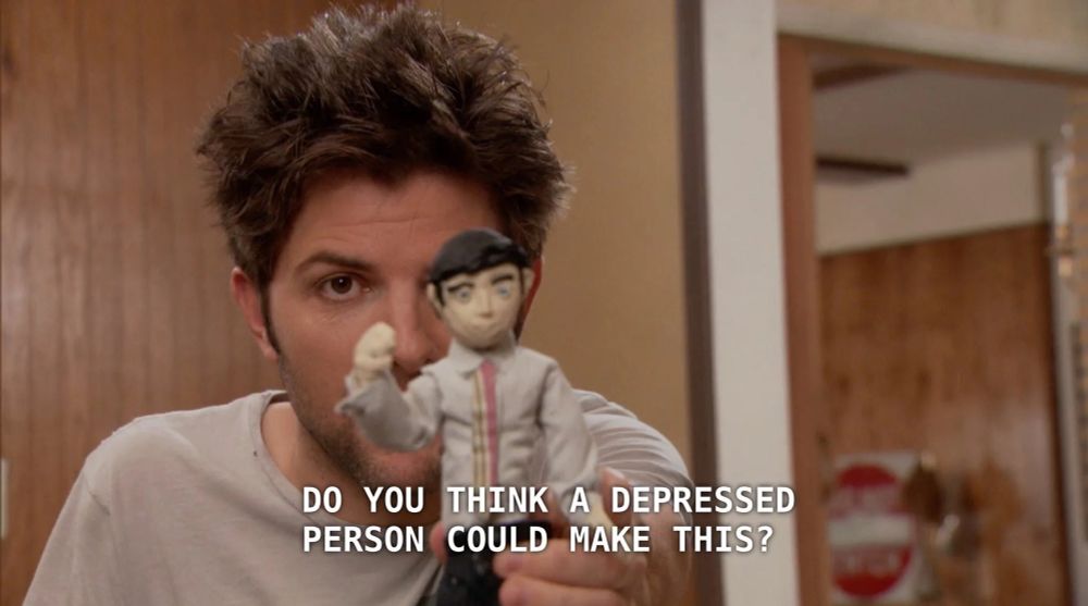 Still of Ben from Parks & Rec, portrayed by Adam Scott, holding up a handmade clay figure of himself with the subtitles saying “Do you think a depressed person could make this?”