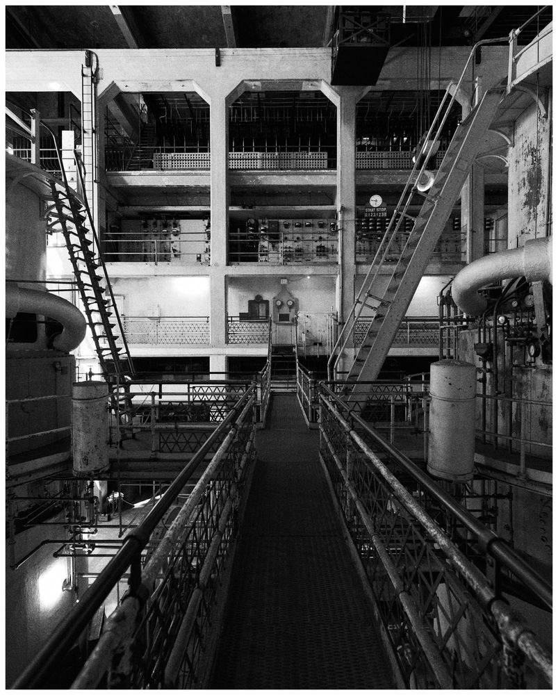 a black and white image showing a catwalk centered between two huge steam generators. several floors at the far end of the room contain offices and electrical gear Nikon D850 24-70