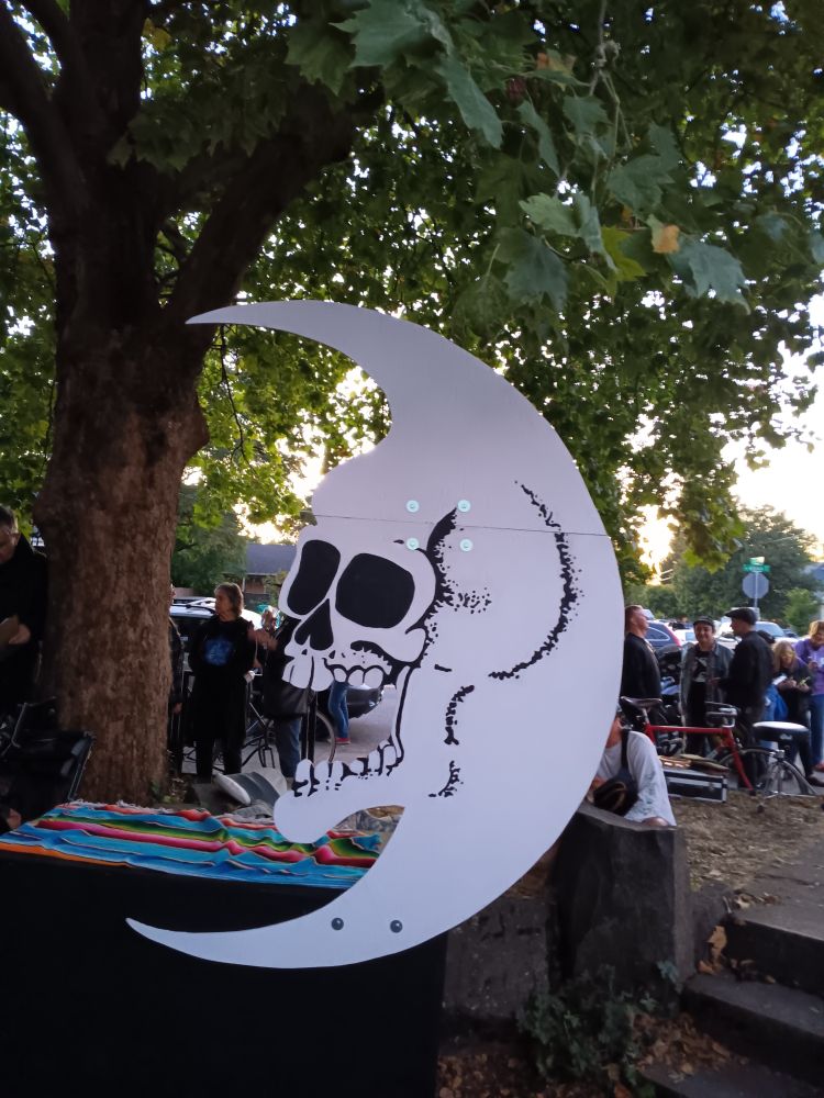 Cut out of the Dead Moon logo set up in a park in Portland. It is a quarter moon with a skull in the middle