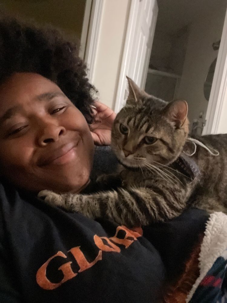 A black woman with an Afro smiling with a cat on her chest