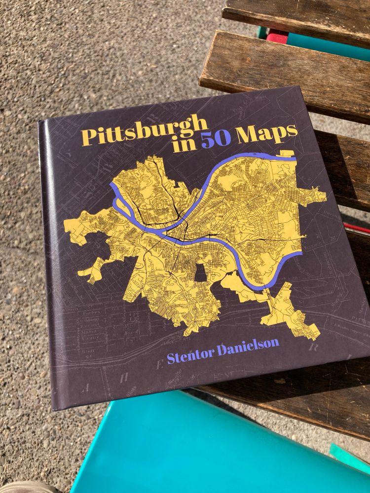 A picture of the book Pittsburgh in 50 Maps by Stentor Danielson sitting on a wooden slat table
