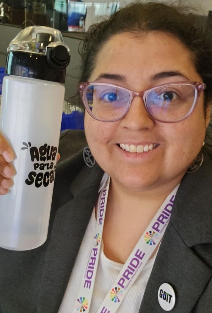 Jenna wearing a gray blazer and a button that says GDIT, holding a water bottle that says Agua pa' la seca