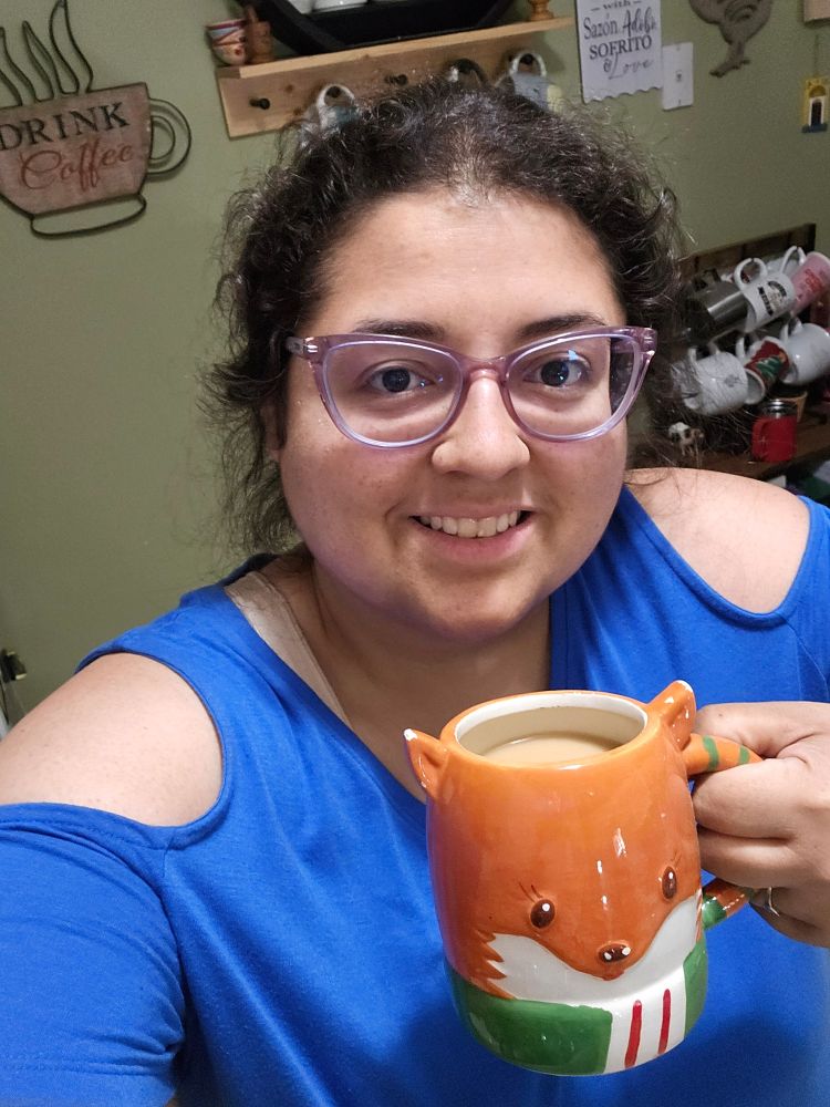 Jenna wearing a blue dress holding a mug of coffee shaped like a fox