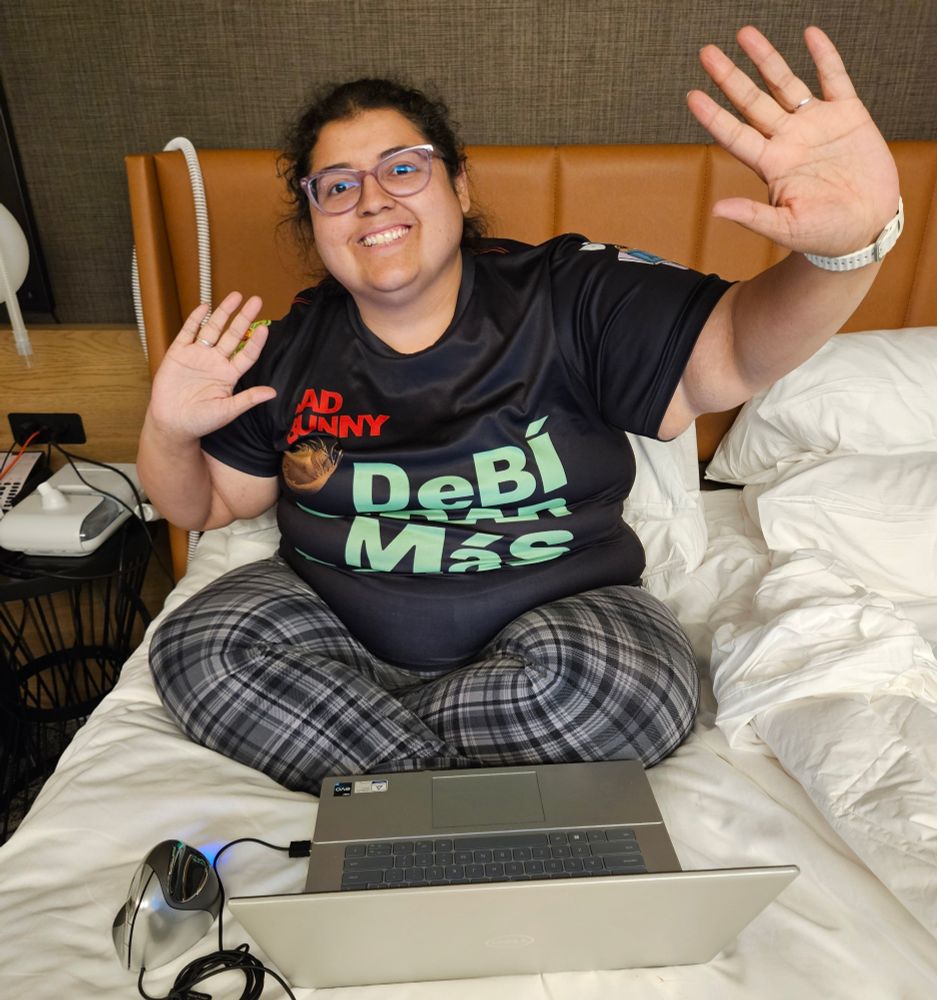 Jenna sitting cross-legged on a bed in front of laptop with her arms raised 
