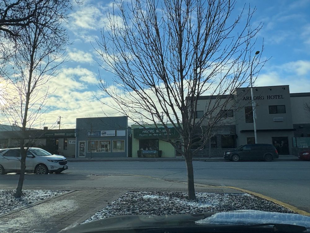 A small Canadian Prairie town Main Street with blue sky overhead. The names on the businesses are Arborg Pharmacy, Arborg Nic-Nacs, and Arborg Hotel.