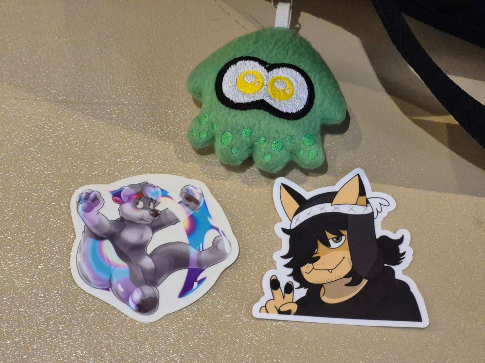 Photo of a gray wolf sticker and a tan dog sticker, with the user's green squid keychain.