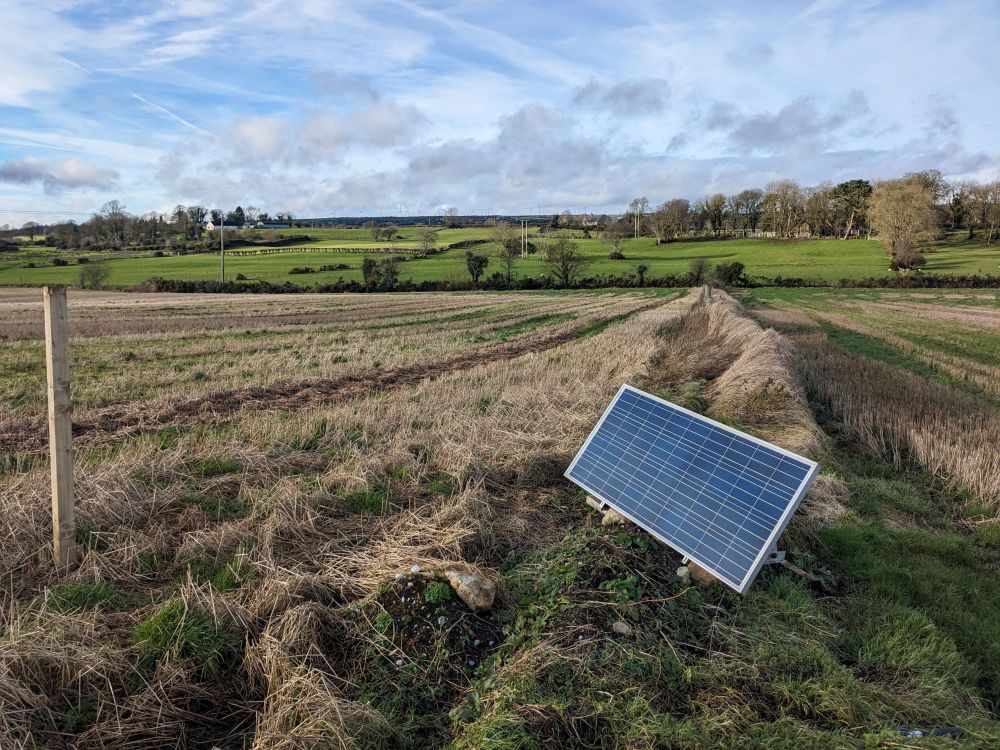 An image of a solar panel in an open field with clear blue skies. The wheat has been cut a few months before.