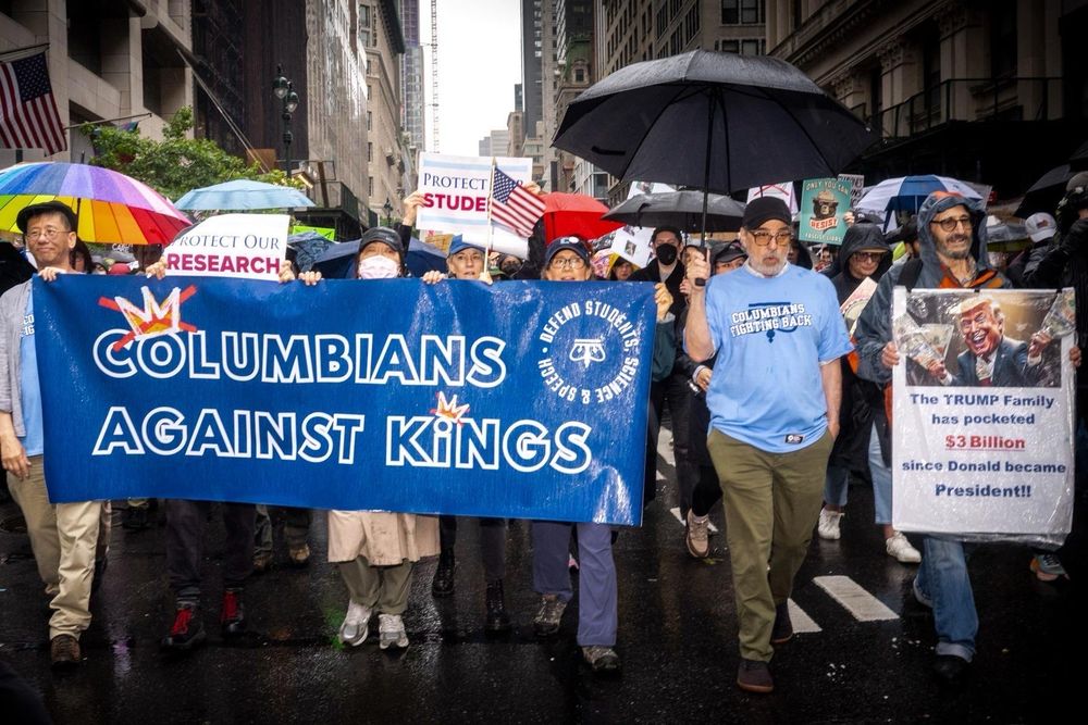 Photo of Columbia contingent at NYC No Kings March with a large sign that says Columbians Against Kings. People are holding umbrellas and wearing rain ponchos. A t shirt in the front says Columbians Fighting Back over an upside down crown.