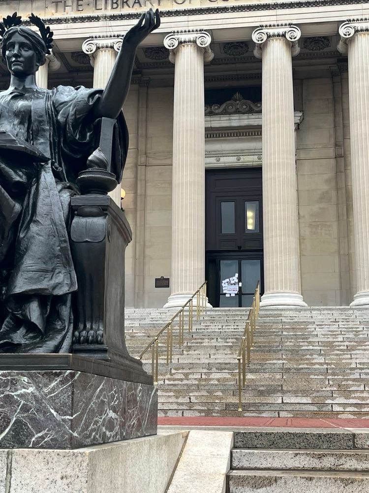 Photo of Low Library at Columbia taken from in front of the Alma Mater statue which is visible to the left, on the right the postcards which were left taped to the door of Low are visible in the background 