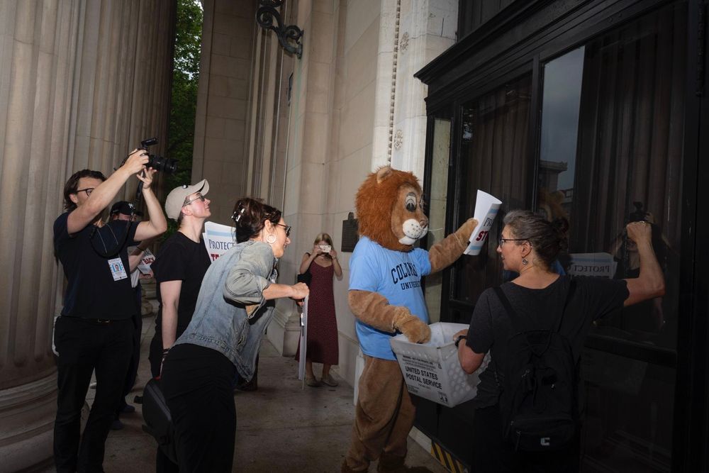 group of faculty and staff and Roaree the lion mascot knocking on the door of low library attempting to deliver the postcards 