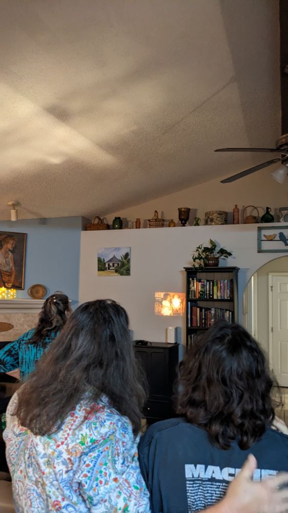 My mother has her arm around my daughter as they watch ild family reels on the wall.