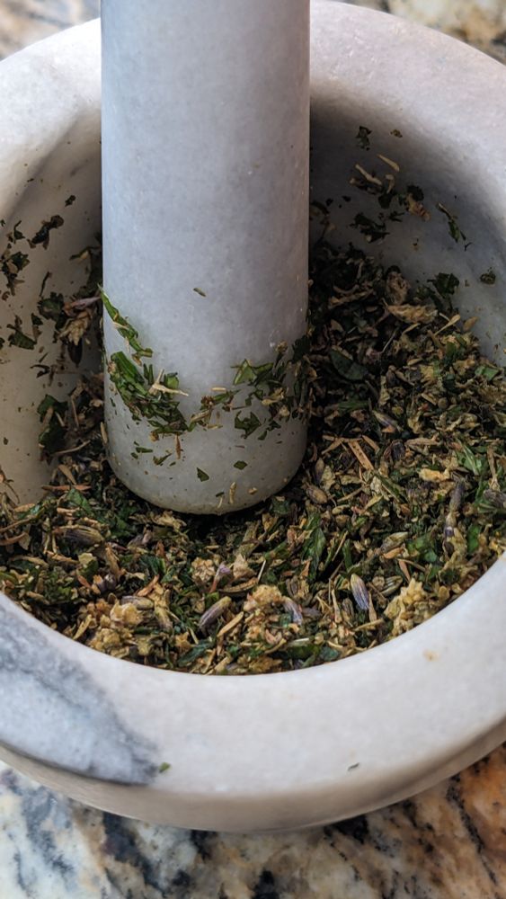 A mixture of fresh and dry herbs sit in a grey and black mortar and pestle, oregano,, basil, lavender, thyme,  marjoram and I added fresh mint. 