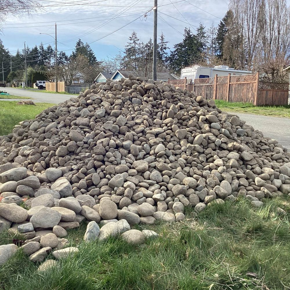 A giant pile of river rocks sitting on an unmowed lawn.