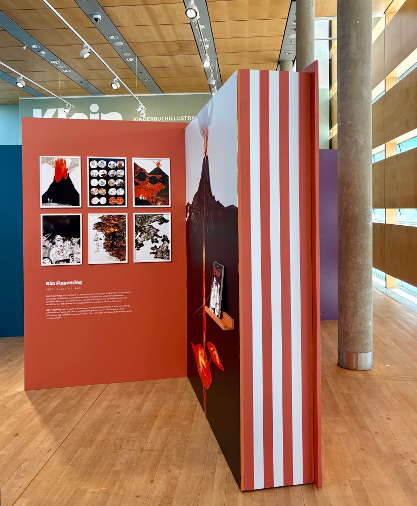 Einblick in die Ausstellung der Kinder- & Jugendbuchillustrationen. Eine Präsentationswand in Form eines geöffneten Buches