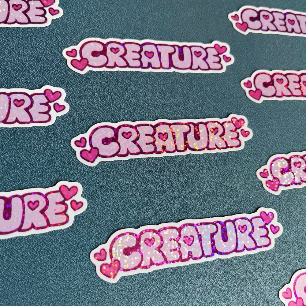 Photo of glittery stickers that depict the word Creature with various little hearts around and inside the word