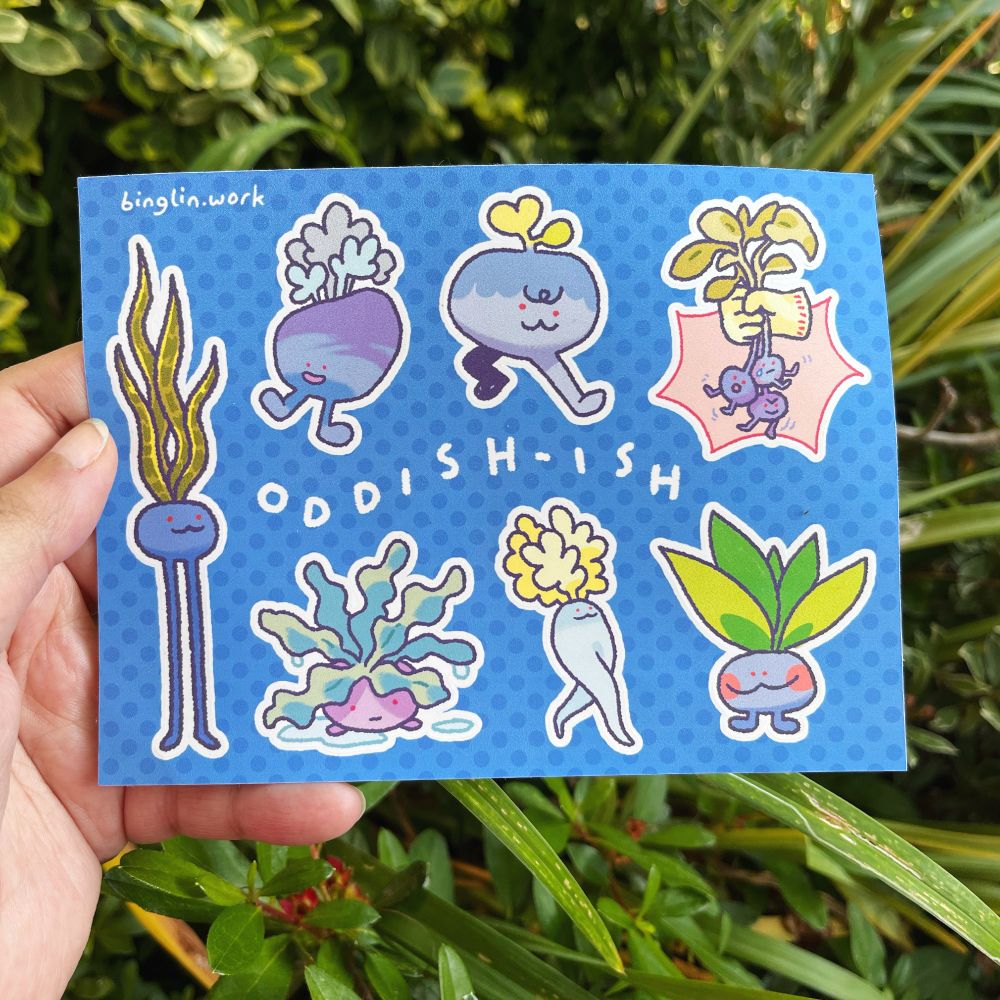 Photo of hand holding the "Oddish-ish" sticker sheet of 7 different off-brand Oddish designs, loosely based on the original Oddish Pokemon design. These designs resemble different plants and root vegetables.