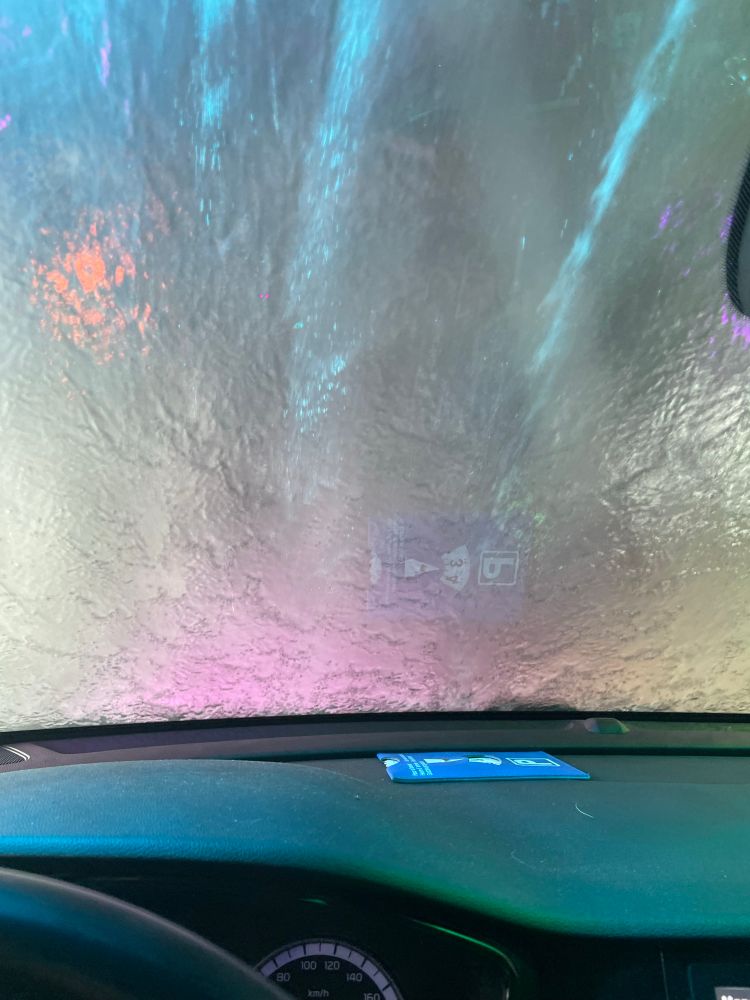 Het dashboard van een auto en de voorruit waar een plens water overheen gaat. 