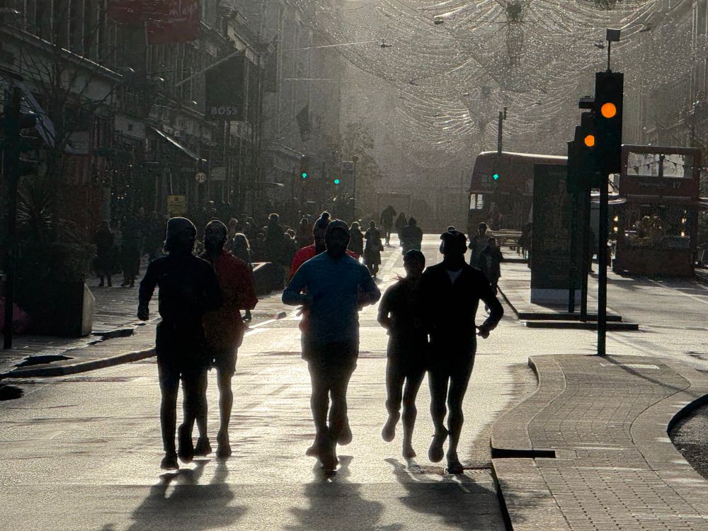 A group of six people running in an empty traffic lane, silhouetted against the low sun