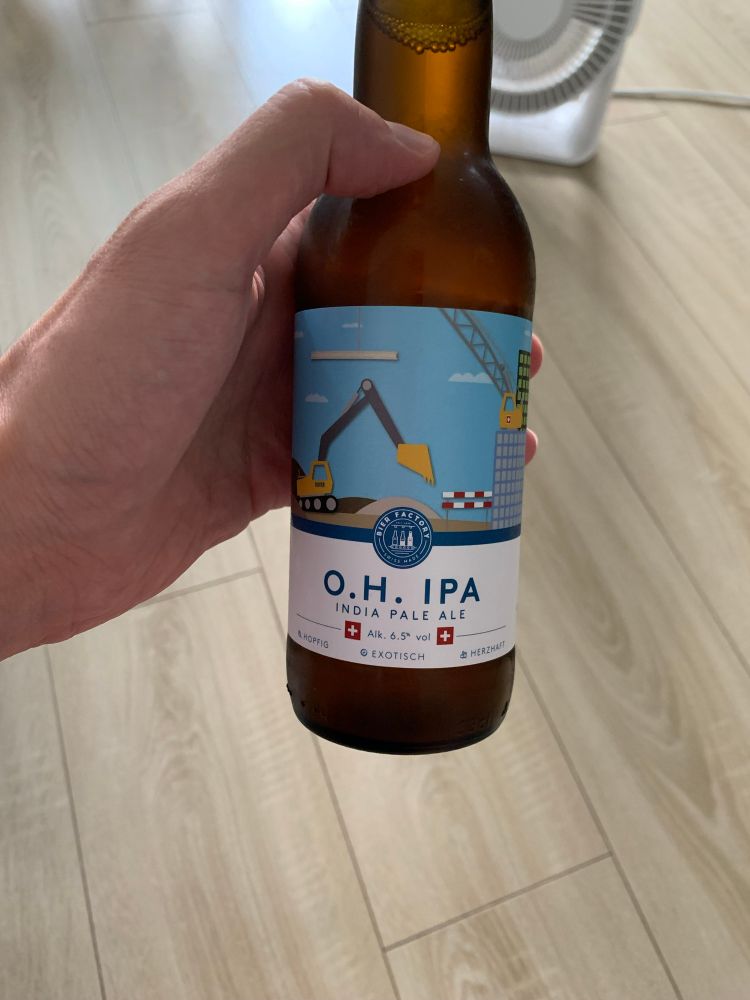 Une bouteille de bière suisse « O.H. IPA » avec un visuel contenant une illustration de travaux avec un tractopelle et un immeuble en construction