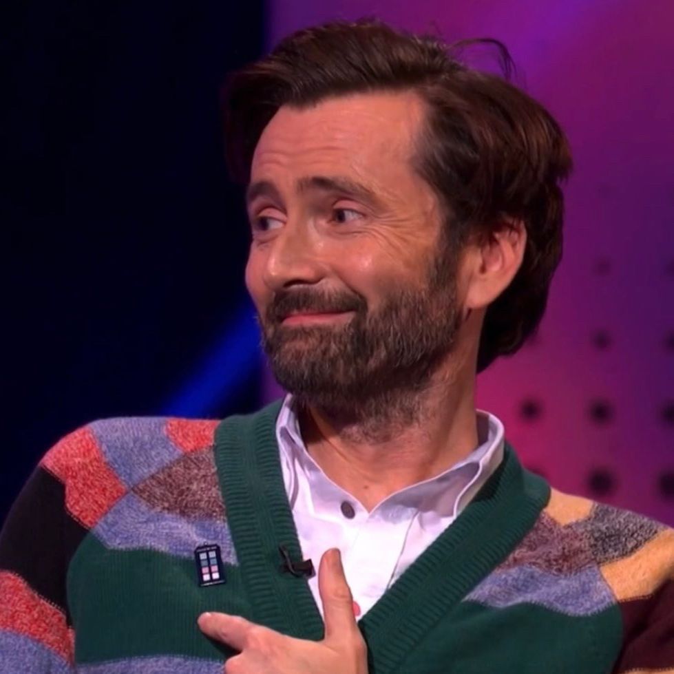 David Tennant pointing to a small pin on his cardigan 
