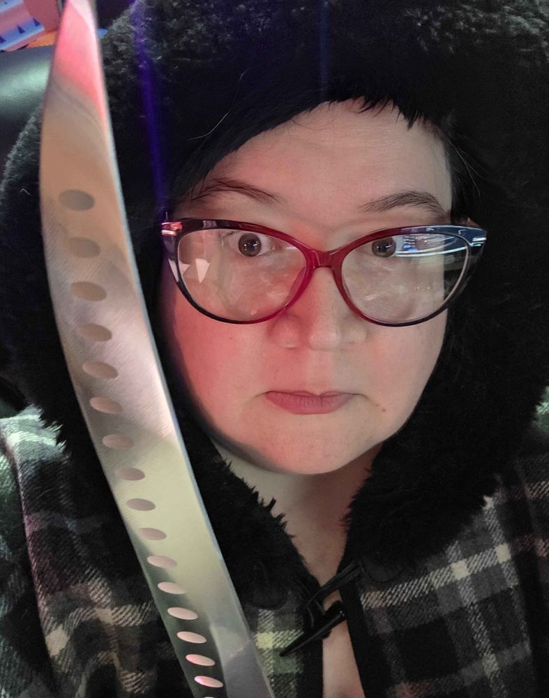 me in a plaid cape with a fur-lined hood holding up a knife that is so big I swear to god you can't see the handle it just looks like I've got a giant murder knife