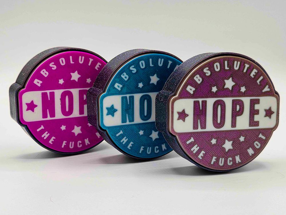 three fidget clickers featuring an old-fashioned vintage label that says NOPE across the middle and "absolutely the fuck not" across the top and bottom, with various stars. They sit in a sparkly black base, and when you press them they click! 