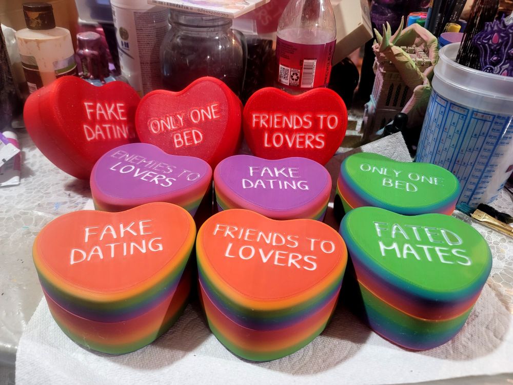 6 more candy heart boxes with romance tropes in the cover. 6 are rainbow colored, and 3 are sparkle red