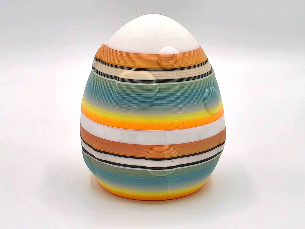 A large egg that splits in half so that you can hide your treasures in it! It's printed in random stripes of white, black, and a orange/gold/green gradient.