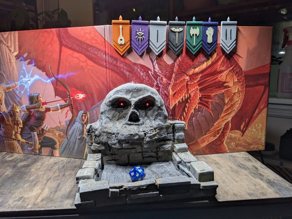 A Skull dice box with glowing red eyes and a twenty sided dice.
