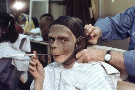 A woman halfway finished with her ape, make up smoking a cigarette on a long holder