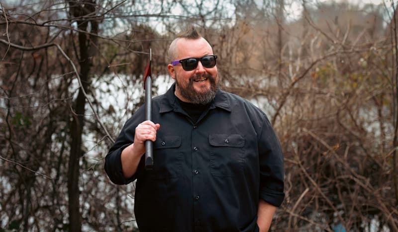 A legend of a man with a mohawk and sunglasses, grinning while holding an ax over his shoulder