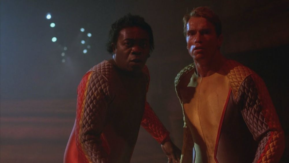 Two men in futuristic leotards looking scared as something approaches them